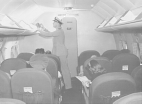 A foreign quarantine officer inspects the overhead storage of plane while the passengers wait in their seats to disembark.