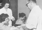 A doctor draws blood from a female patient while a nurse stands watching.