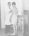 At the Naples Foreign Quarantine Station Dr. Franco Ermenegildo stands and examines the chest and heart of 27-year-old Ferdinando De Panlis from Bagno, Italy who is wearing only underwear.