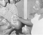 A man administers an oral polio vaccine to a child being held by its mother.