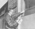 Public Health Service officer Gail Schmidt checking the level of contamination on the exterior of a building used by radium source manufacturer and importer in New York, Canadian Radium-Uranium Div.