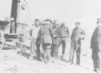 Five men stand near a covered wagon while a scientist checks them for spotted fever.