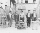 Group portrait of six male rat-proofing volunteers posing with rat traps, cages, and rat collection buckets during the Public Health Service campaign against the New Orleans' plague epidemic of 1914-1920.