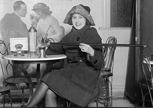 Woman sitting in café pouring alcohol into her glass from a hollowed out cane.
