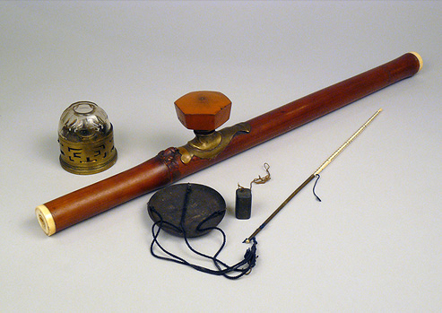 Photograph of an Opium pipe, metal and glass lamp, scale and weigh.