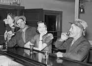 Black and white photograph of four people drinking alcohol at a bar.