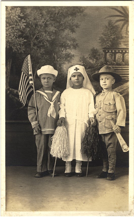 Three White children the girl is dressed as a nurse; the boys as soldier and sailor.