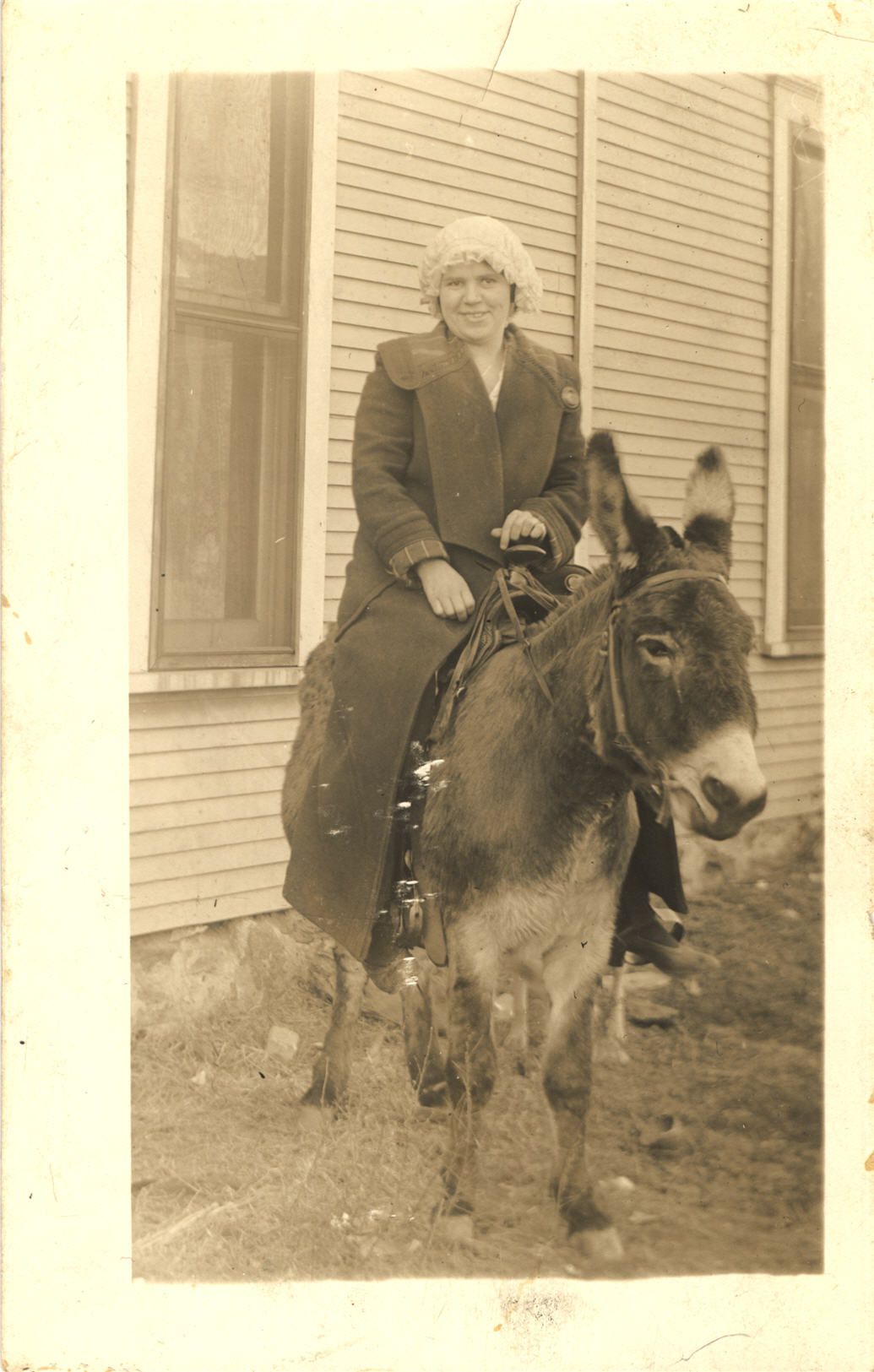 A White female nurse sitting on top of a donkey and smiling at the viewer.