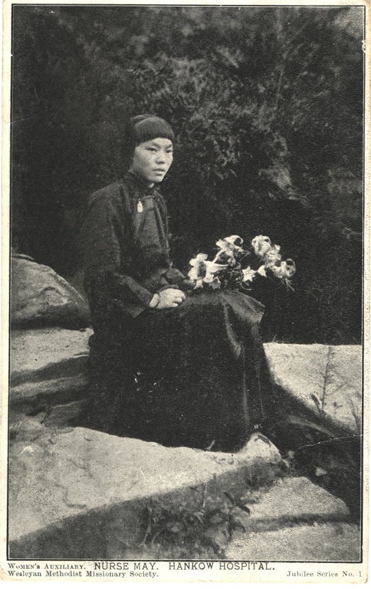 A Chinese female nurse in black, sitting with flowers on her lap.