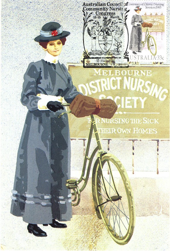 White female nurse in blue, standing holding a bike, looking at viewer.