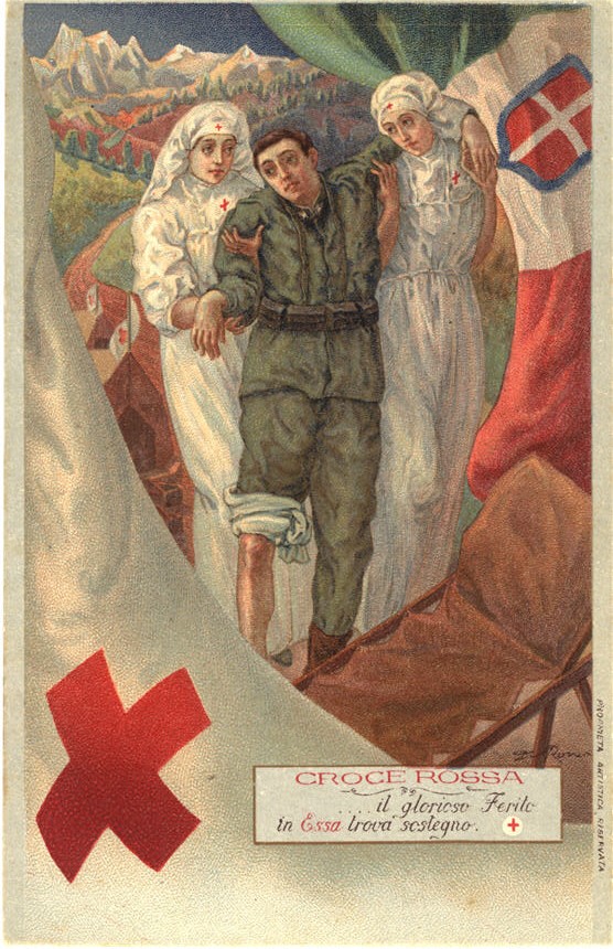 Two White female nurses support a wounded White man as he walks to a stretcher at a field hospital.