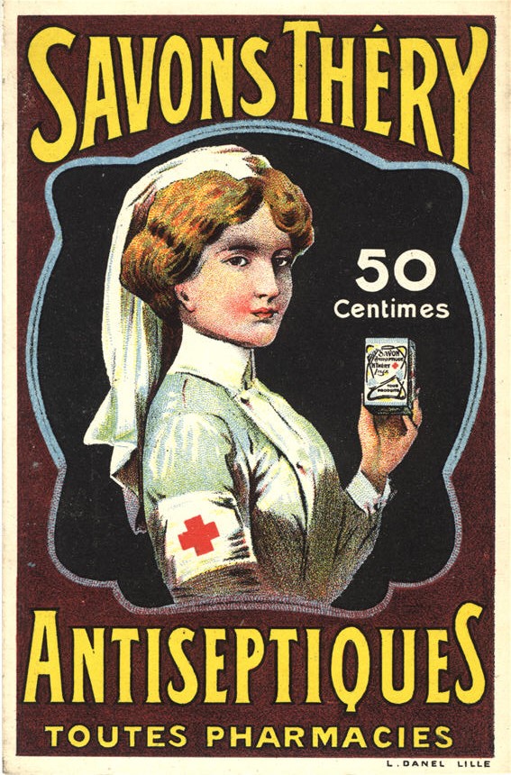 A White female nurse in white holds a box of medicine and looks at the viewer.