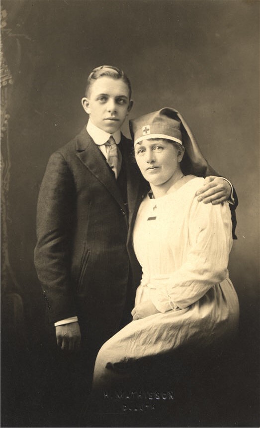 A White female nurse sitting beside a White teenage boy in a suit.