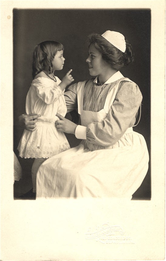 A White female nurse sitting, facing a White girl who stands on the seat next to her.
