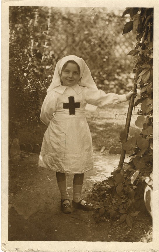 A white girl dressed in a Red Cross nursing uniform, standing in a garden.