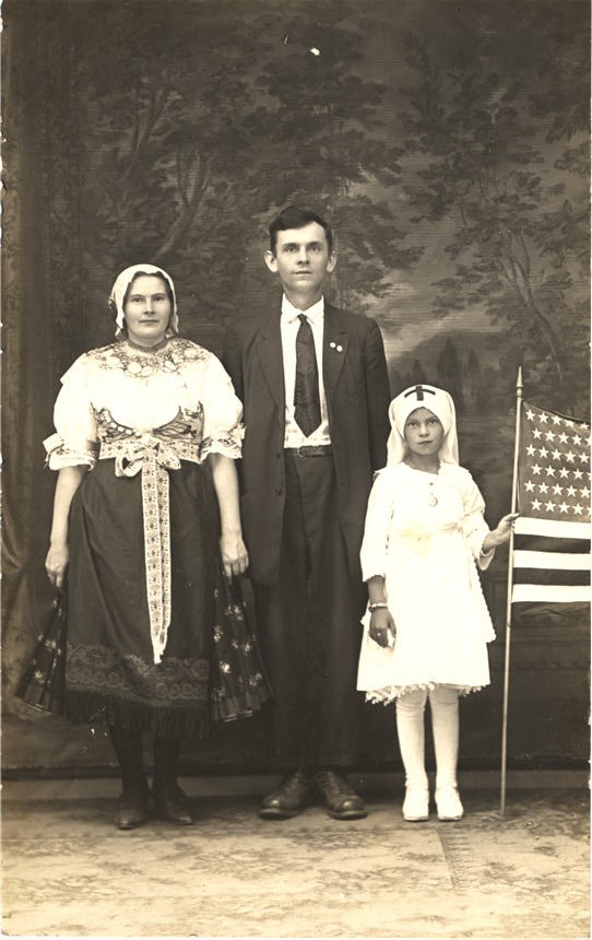 A White man, woman, and girl facing the viewer. The girl is dressed as a nurse and holding a flag.