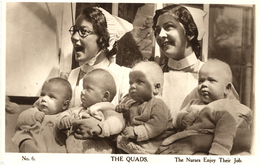 Two White female nurses, holding two white babies each. They are both smiling.