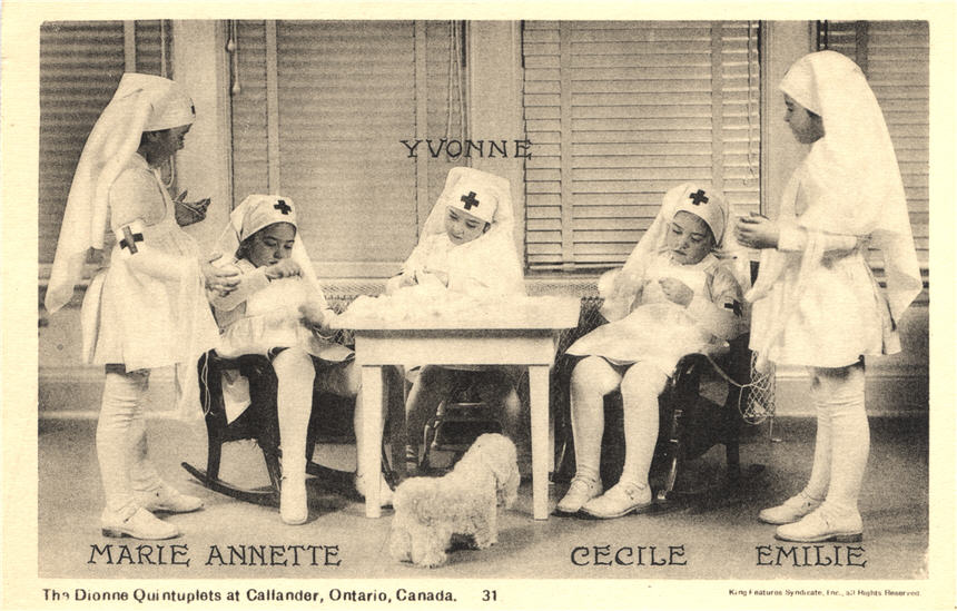 Five White girls dressed as nurses in white, sitting and standing around a small table.