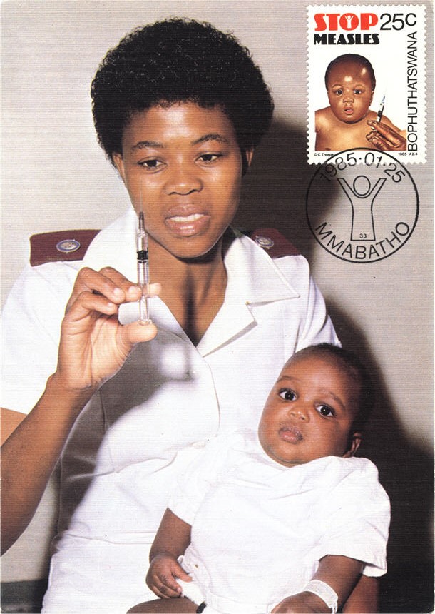 African nurse holding a syringe and an African baby in her arms.