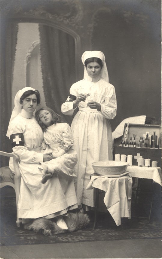 Two White female nurses, one is holding an ill White girl in her lap.