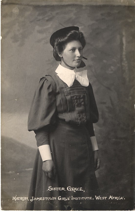 White female nurse in a gray uniform and hat with large white bow around neck.