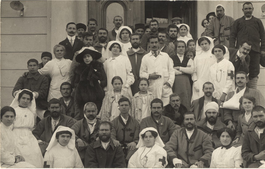 Large group of White men and women on the front steps of a hospital, including nurses in white.