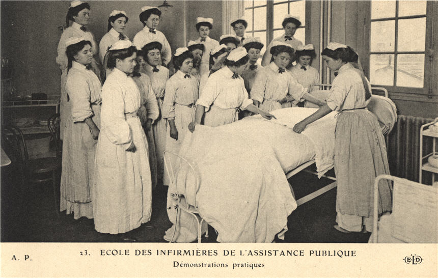 A group of White female nurses in white watch three others demonstrate bed making.