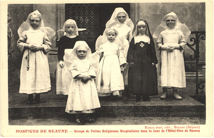 Seven White girls dresses as nun nurses in white and black stand in front of a hospital.