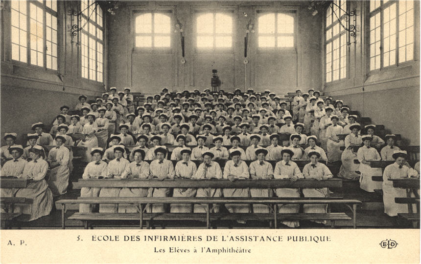 A large group of White female nurses in white sit in a rows of seats in an auditorium.
