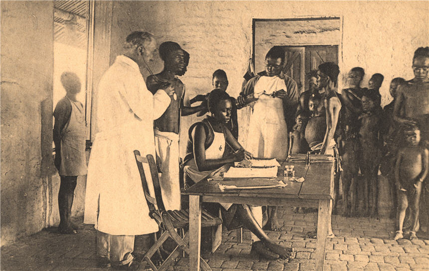 A White male doctor and three African female nurses in white aprons tend to African patients.