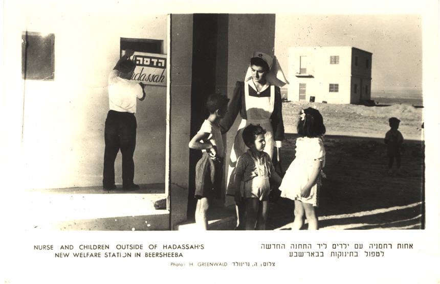 A White female nurse in white apron with four White children stand next to a health clinic.
