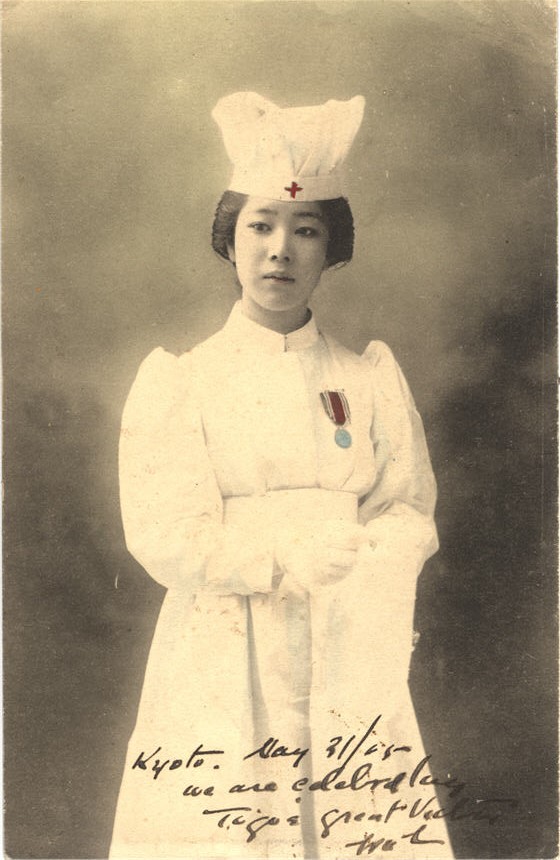 An Asian female nurse in white, wearing war medal, looking slightly off to the left.
