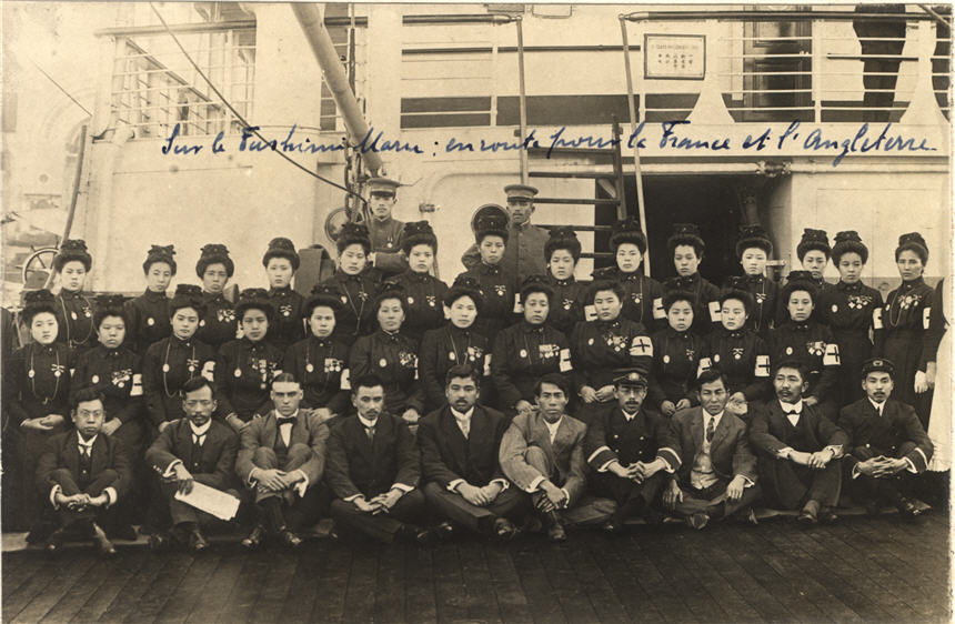 A large group of Asian female nurses and male support staff sit for a group photograph on a ship.