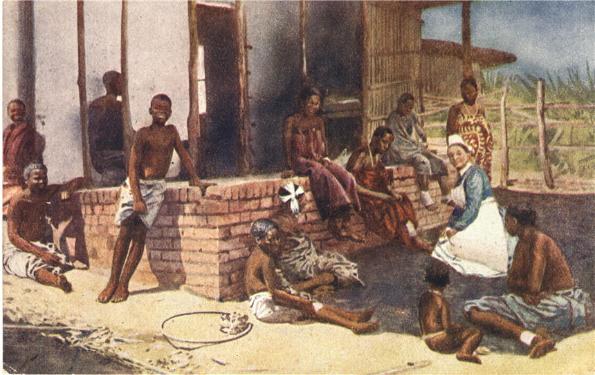 A White female nurse in blue and white, among a group of twelve Africans in front of a building.