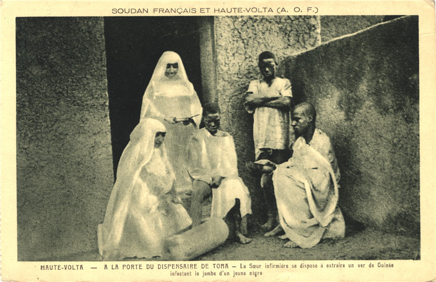 Two White nun nurses and an African male assistant tend to an African boy as another boy looks on.