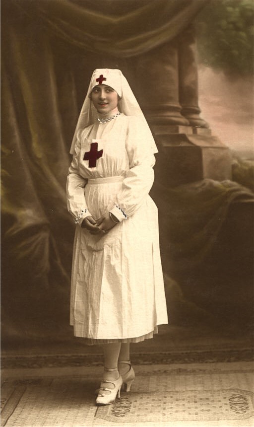 A White female nurse in white stands and looks slightly off to the right.