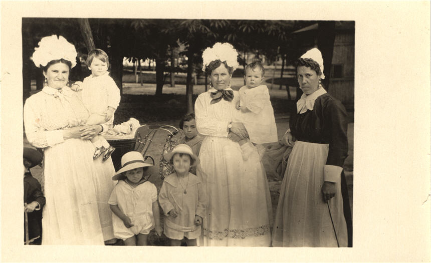 Three White female nurses in white and black with six White children, look at viewer.