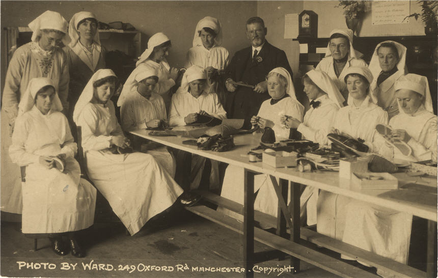 Fourteen White female nurses in white and a White man, stand and sit around a table working.