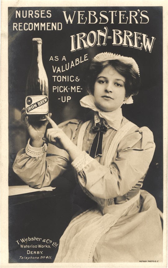 White female nurse sitting and looking at the viewer while pointing at a bottle she is holding.