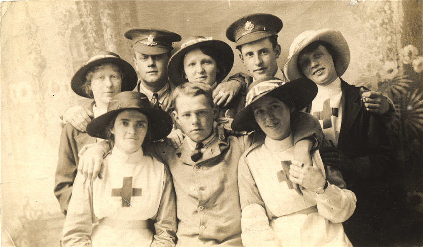 Five White female nurses in white stand for a photograph with three White male soldiers.