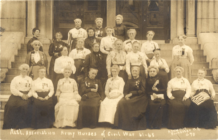 Large group of elderly White women wearing medals sitting and standing in front of a building.