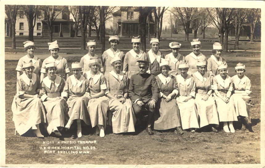 Nineteen White female nurses in white sit and stand for a group photo with a White male officer.