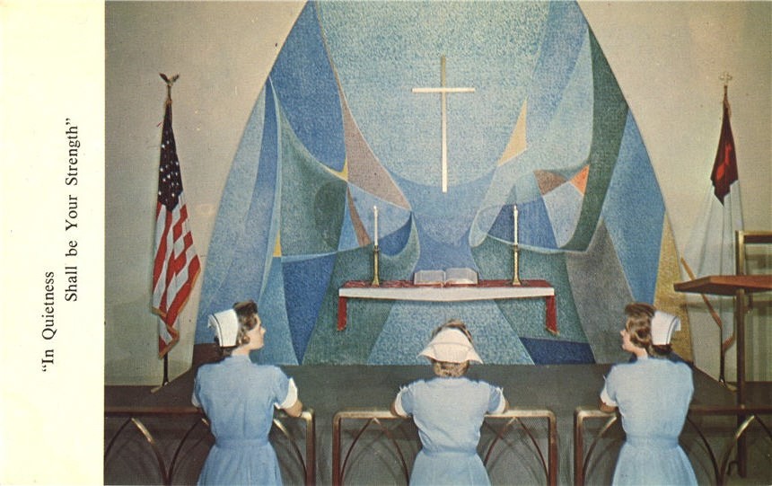 Three White female nurses in blue kneel and pray in a church.