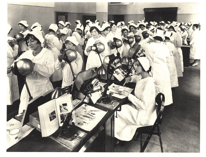 Room full of White female nurses in white at dental stations working on dummies.