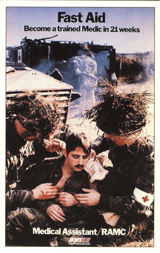 Two White male medics in camouflage tend to a wounded White male soldier next to a vehicle.