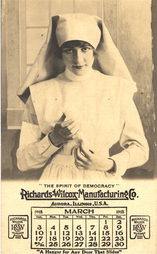 A White female nurse in white visible from the waist up looking at the viewer above a calendar.