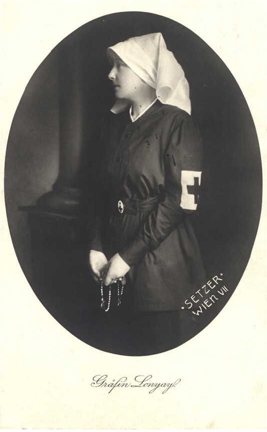 A White woman (Countess Lonyay) in black wearing a Red Cross armband looking to the left.