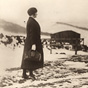A White woman in all black with a nursing bag in her hand walking in the snow.
