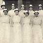 Nine African American female nurses in white standing in a group looking at the viewer.
