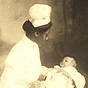 African American female nurse holding a White infant in a basket on her lap.